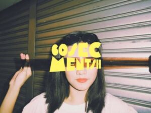 A person in a white shirt holds a strip of photographic film in front of a metal shutter, with the bold yellow lettering "60 SEC MENTSH UNITED" partially obscuring their face.